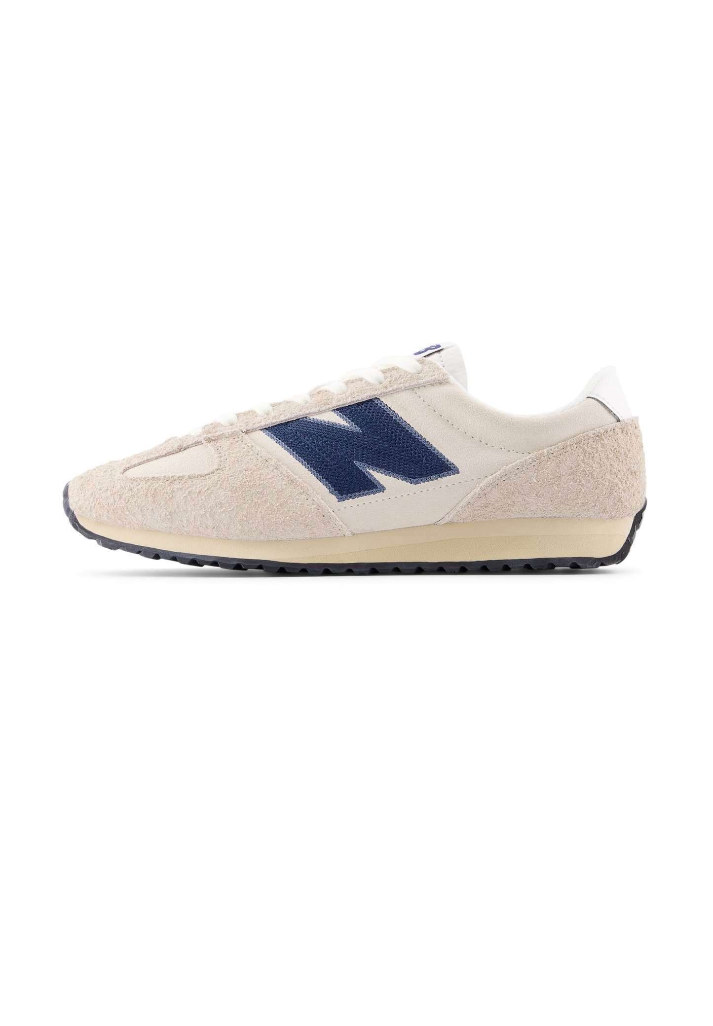 Zapatilla con parte superior de ante beige y malla, logo "N" azul marino, lengüeta trasera blanca y suela de goma negra. Diseño con cordones y detalles sutiles de textura.