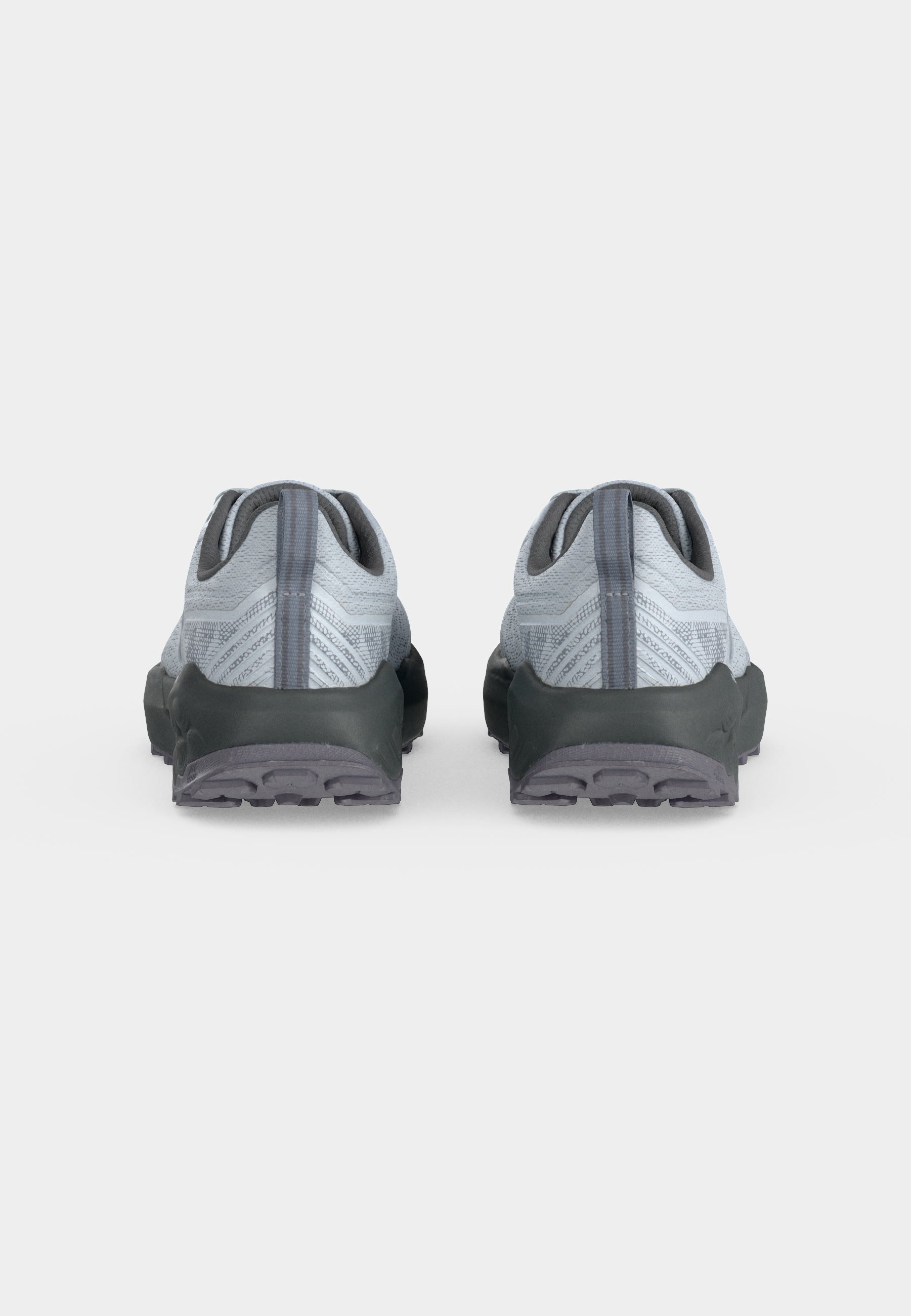 Par de zapatos deportivos grises con partes superiores de tela texturizada y suelas negras gruesas, mostrados desde atrás sobre un fondo blanco liso.