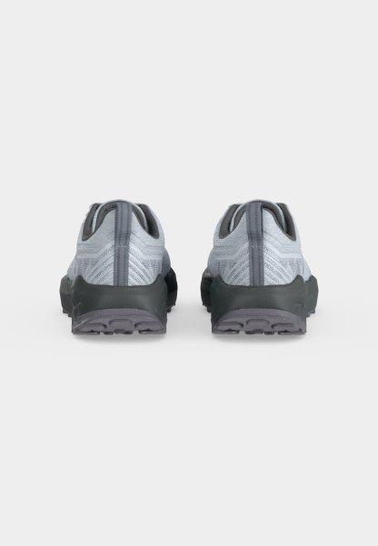 Par de zapatos deportivos grises con partes superiores de tela texturizada y suelas negras gruesas, mostrados desde atrás sobre un fondo blanco liso.