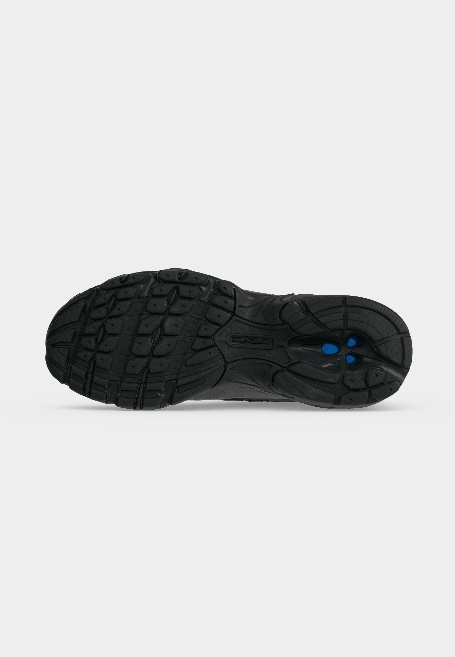 Suela de zapato de goma negra con patrón de dibujo texturizado y detalles circulares azules cerca del talón sobre un fondo gris liso.