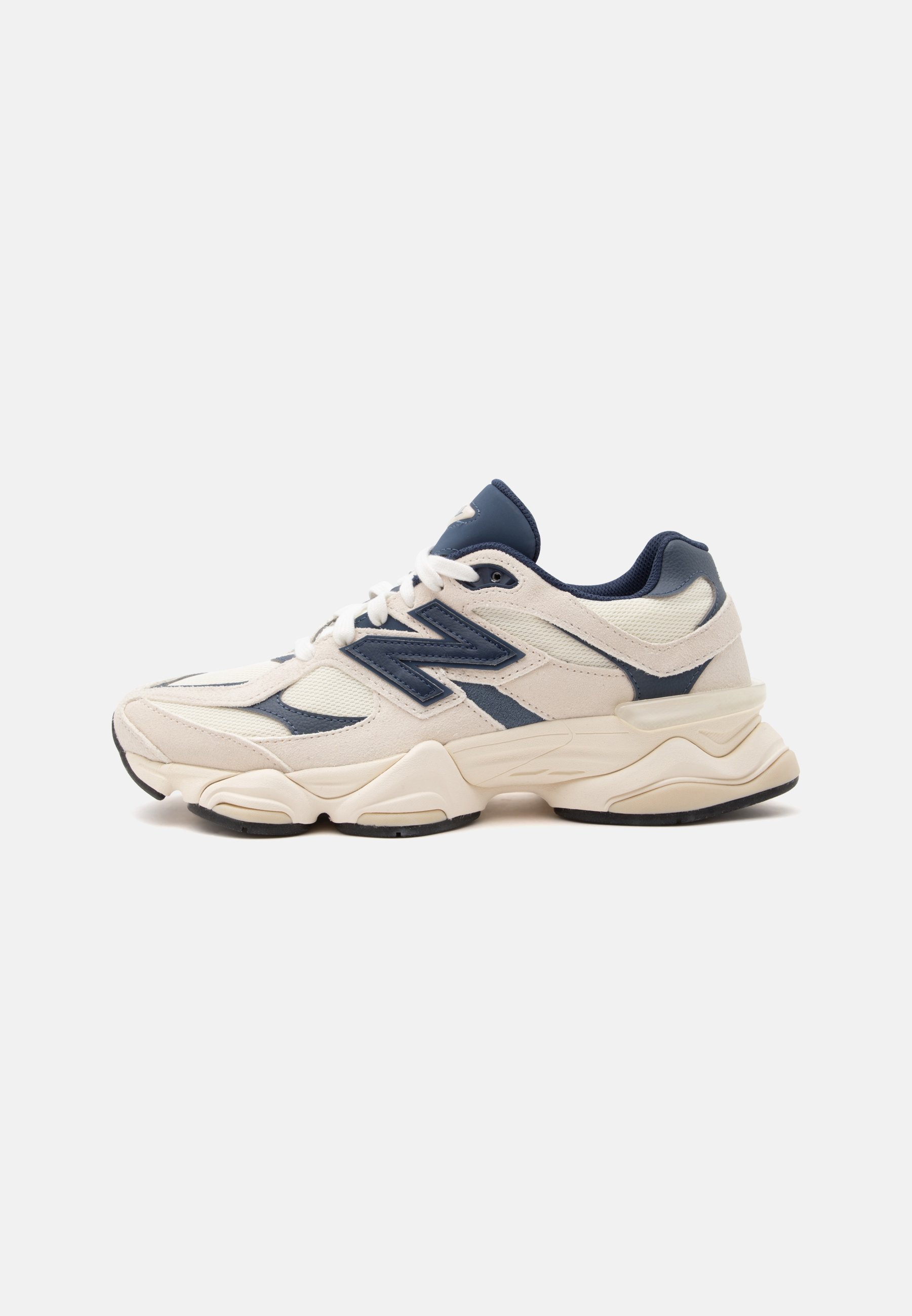 Zapatilla New Balance blanca y azul marino con suela gruesa, parte superior de malla y cuero, y cordones blancos sobre un fondo claro y liso.