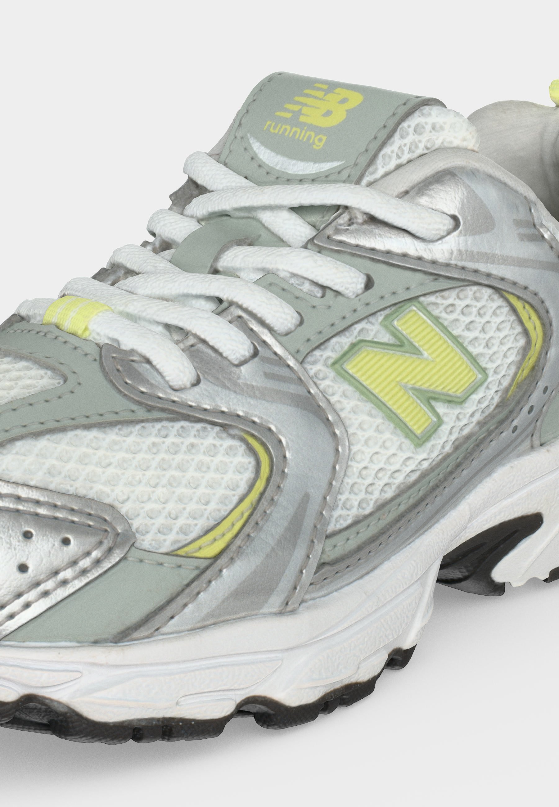 Zapatilla de running New Balance en gris, blanco y amarillo con tejido de malla, cordones y suela texturizada, mostrada de cerca.