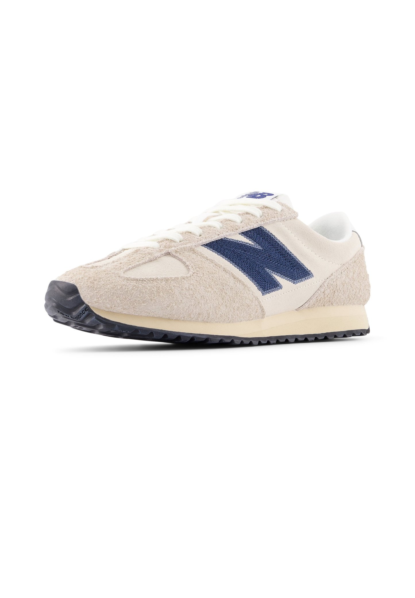 Zapatilla de ante beige con detalles en azul marino, diseño con cordones y parte superior texturizada. Cuenta con suela de goma negra para tracción. Estilo atlético clásico.