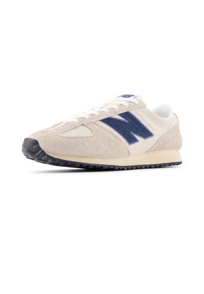 Zapatilla de ante beige con detalles en azul marino, diseño con cordones y parte superior texturizada. Cuenta con suela de goma negra para tracción. Estilo atlético clásico.