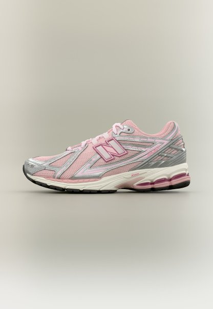 Zapatilla de running New Balance en rosa y plata con parte superior de malla, suela acolchada y logotipo "N" en el lateral, mostrada sobre fondo gris.