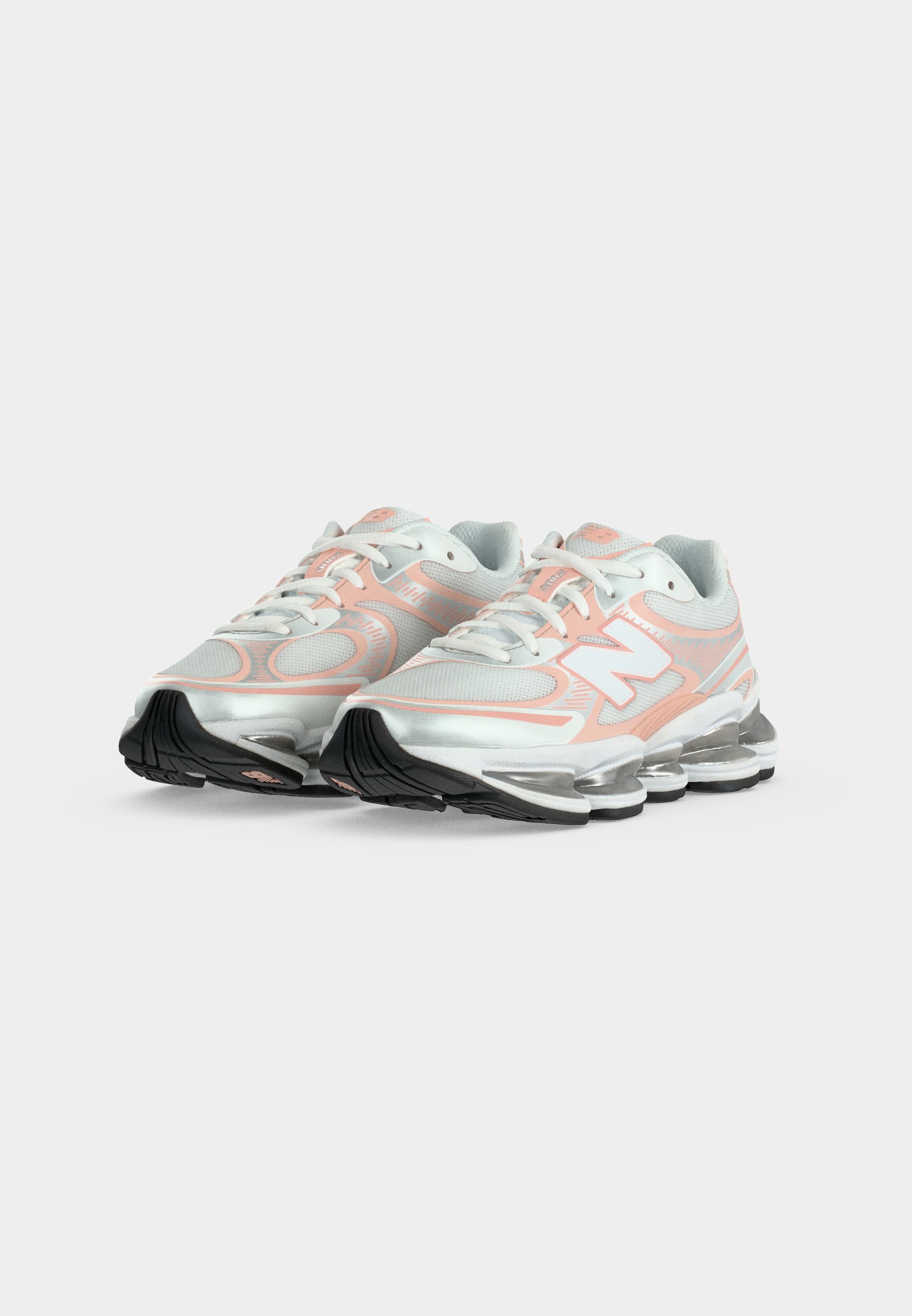 Par de zapatillas deportivas blancas y rosa pálido con tejido de malla, suelas acolchadas y suelas exteriores negras inclinadas hacia adelante sobre un fondo liso.