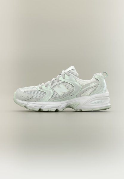 Zapatilla deportiva blanca y gris claro con paneles de malla, diseño con cordones y suela acolchada etiquetada con "ABZORB" sobre un fondo neutro.