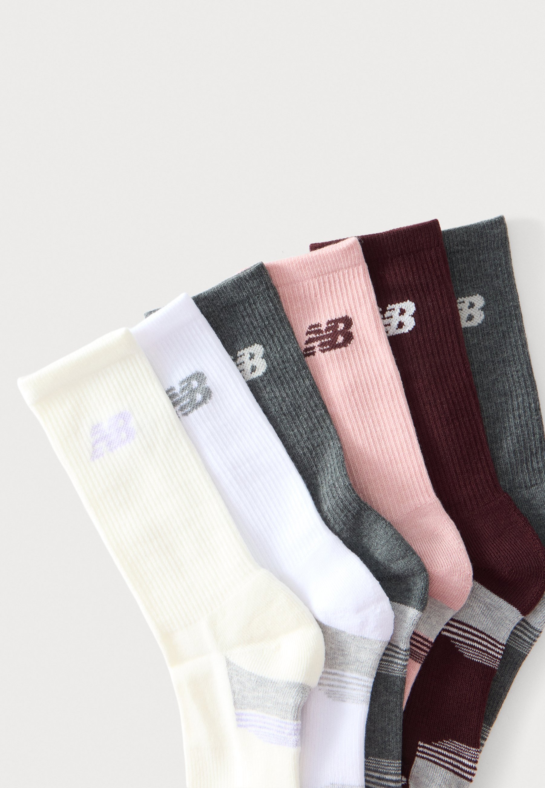 Seis pares de calcetines New Balance tipo crew en blanco, gris, rosa, granate y gris oscuro, dispuestos superpuestos sobre un fondo claro.