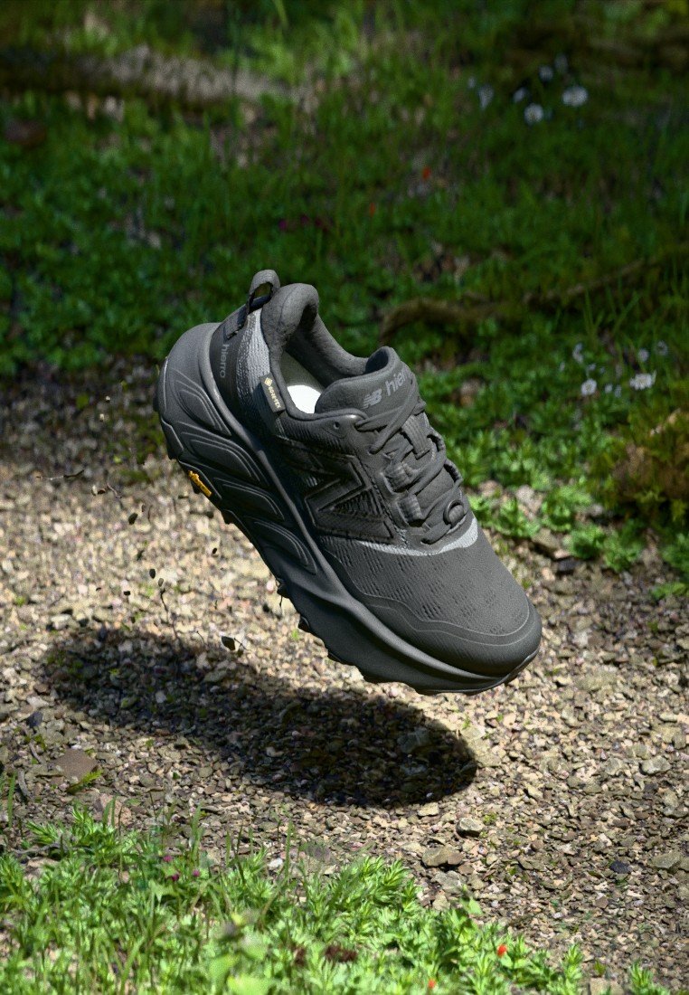 Zapato de senderismo negro con parte superior texturizada, sistema de cordones y suela acolchada; diseño ligero con marca visible y acentos de goma.