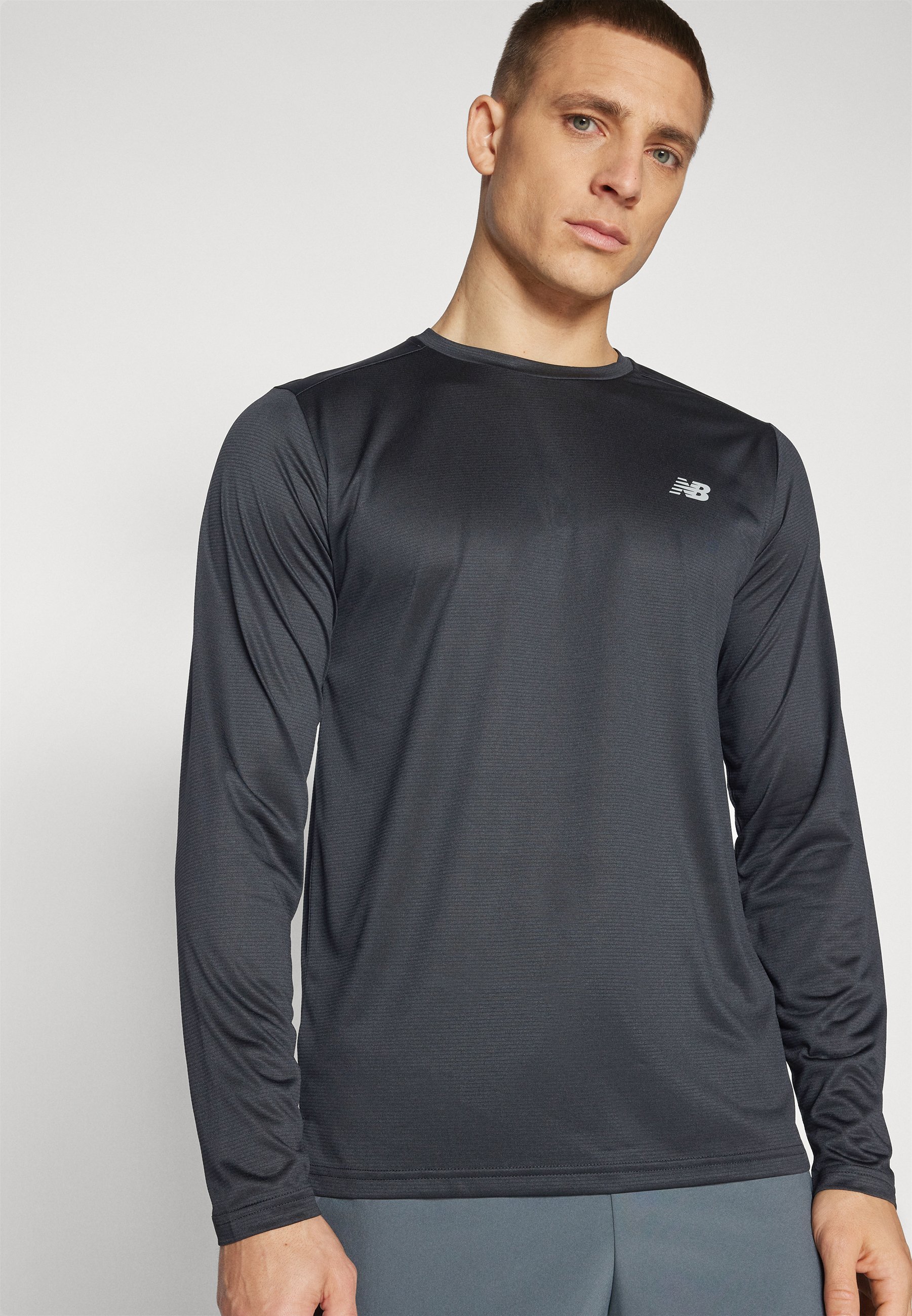 Camisa atlética de manga larga en gris oscuro, hecha de una tela ligera y suave con una textura sutil; presenta un pequeño logo blanco en el pecho.