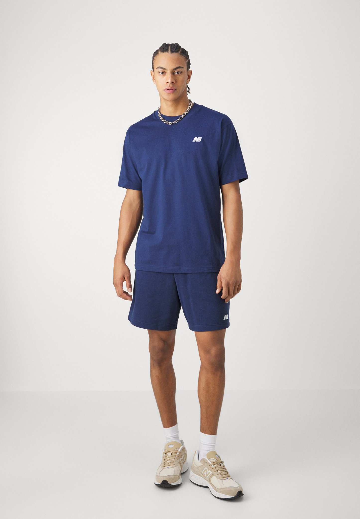 Camiseta de algodón azul marino de manga corta y cuello redondo, combinada con pantalones cortos a juego. Logo blanco en el pecho y en los pantalones cortos. Zapatillas neutras.