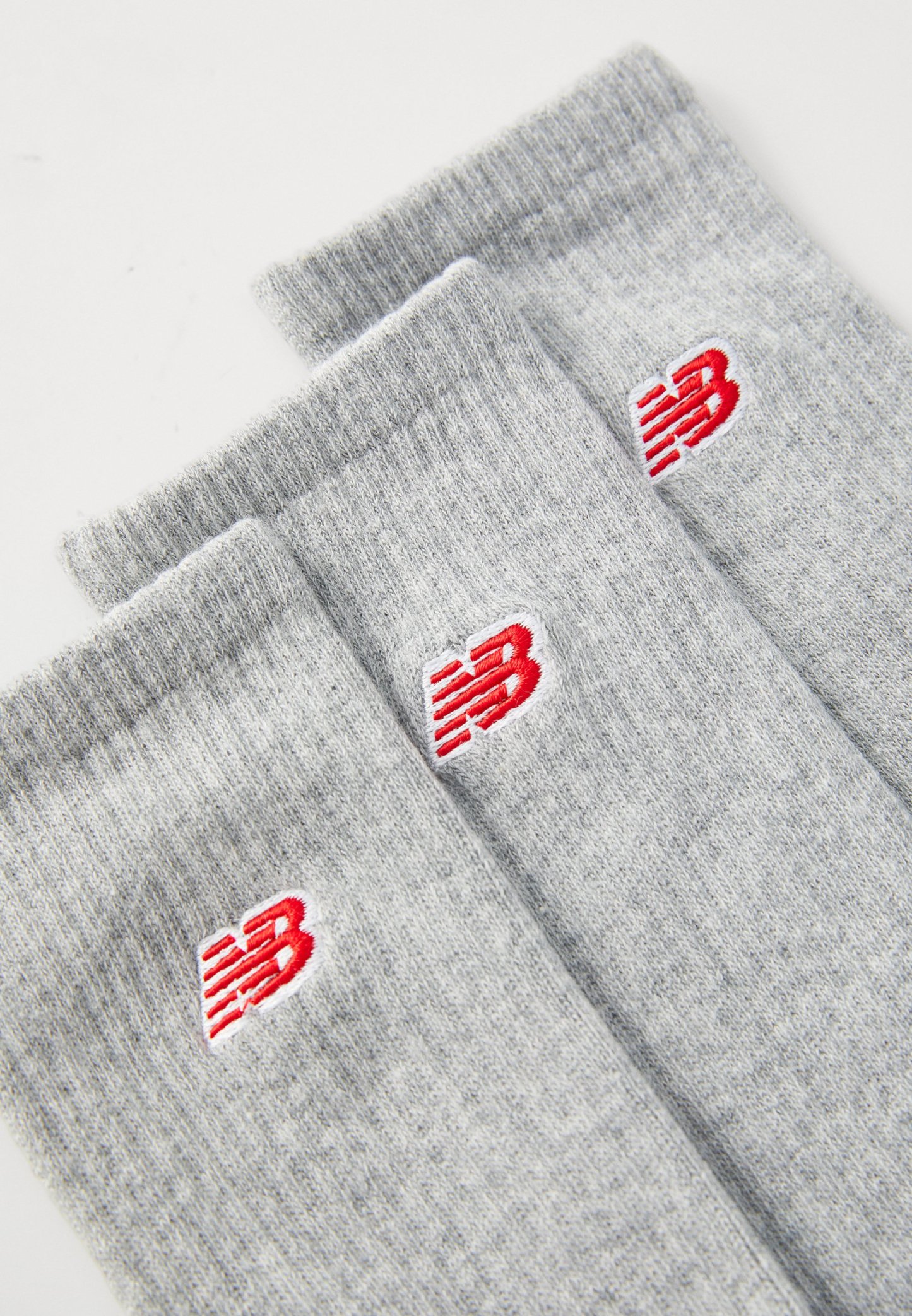 Tres pares de calcetines de algodón gris claro con puños acanalados, presentando un logo rojo en cada calcetín. La textura es suave y de punto.