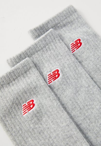 Tres pares de calcetines de algodón gris claro con puños acanalados, presentando un logo rojo en cada calcetín. La textura es suave y de punto.