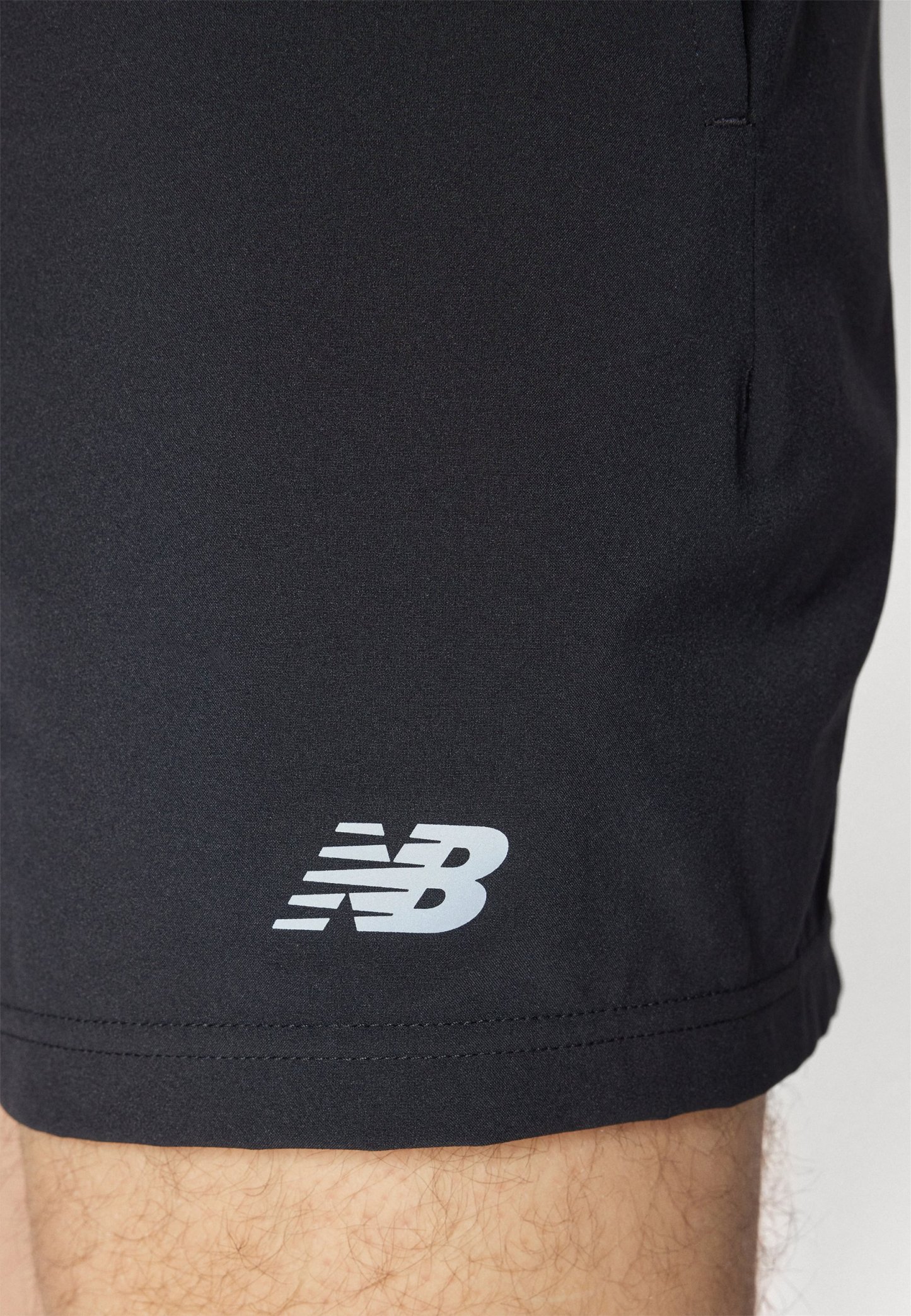 Shorts atléticos negros fabricados con un tejido suave y ligero. Presentan un logo blanco de New Balance cerca del dobladillo y bolsillos laterales.
