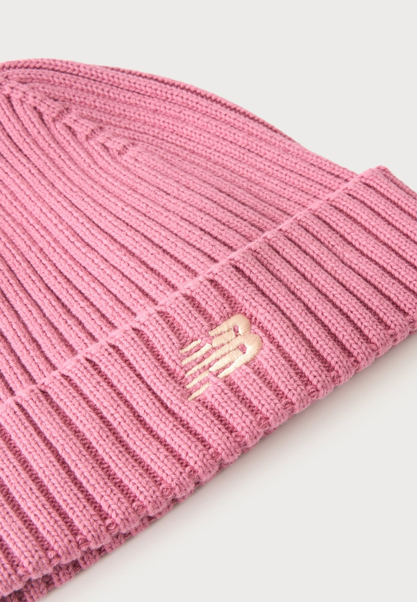Gorro de punto acanalado rosa con puño doblado y pequeño logo bordado en rosa claro en el puño sobre un fondo blanco.