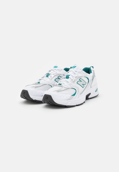 Zapatillas deportivas blancas con acentos en verde azulado, parte superior de malla, punta redondeada, suela acolchada y cordones blancos. Presentan un logo en el lateral y una suela duradera.