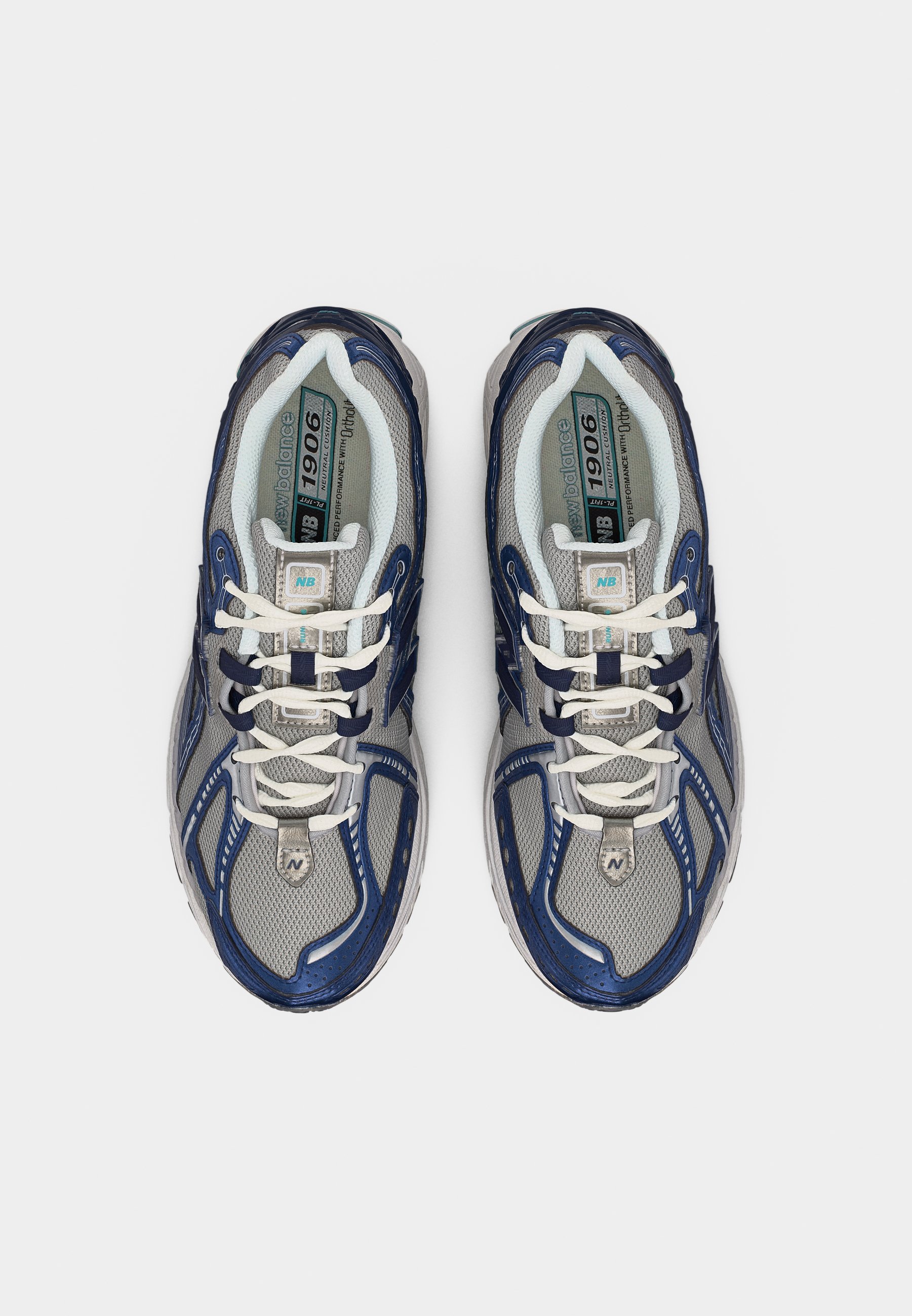 Par de zapatillas para correr New Balance 1906 en gris y azul marino con cordones blancos, vista desde arriba sobre un fondo liso.