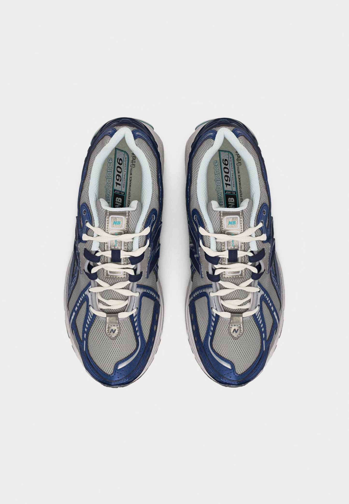 Par de zapatillas para correr New Balance 1906 en gris y azul marino con cordones blancos, vista desde arriba sobre un fondo liso.