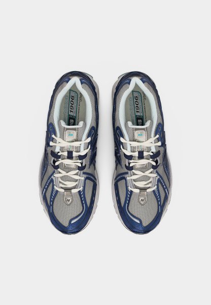 Par de zapatillas para correr New Balance 1906 en gris y azul marino con cordones blancos, vista desde arriba sobre un fondo liso.