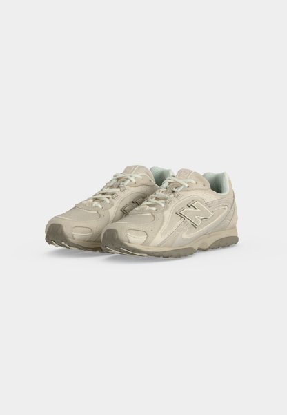 Par de zapatillas New Balance beige con cordones blancos y detalles grises, colocadas una al lado de la otra sobre un fondo blanco.