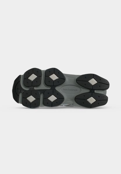 Suela de zapato New Balance gris y negro con dibujos en la banda de rodadura y zonas de agarre blancas en forma de diamante sobre fondo blanco.