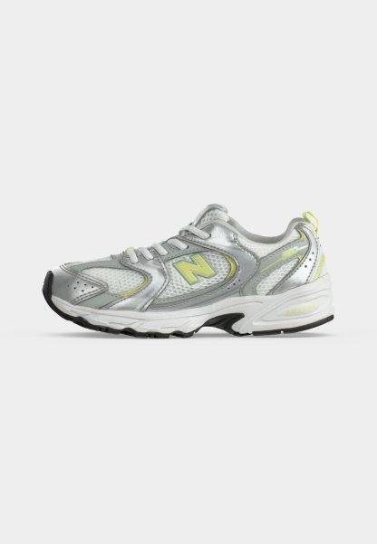 Zapatilla de running plateada y blanca con detalles verde claro y suela negra, con un gran logo "N" en el lateral.