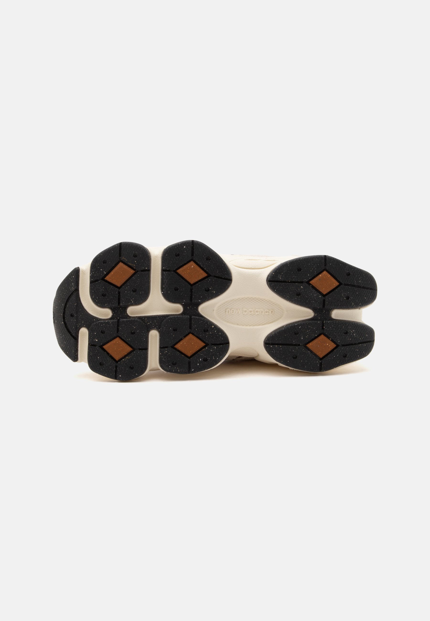 Suela de una zapatilla con tacos de goma segmentados en negro y marrón sobre una base beige, mostrando el nombre de la marca en relieve en el centro.