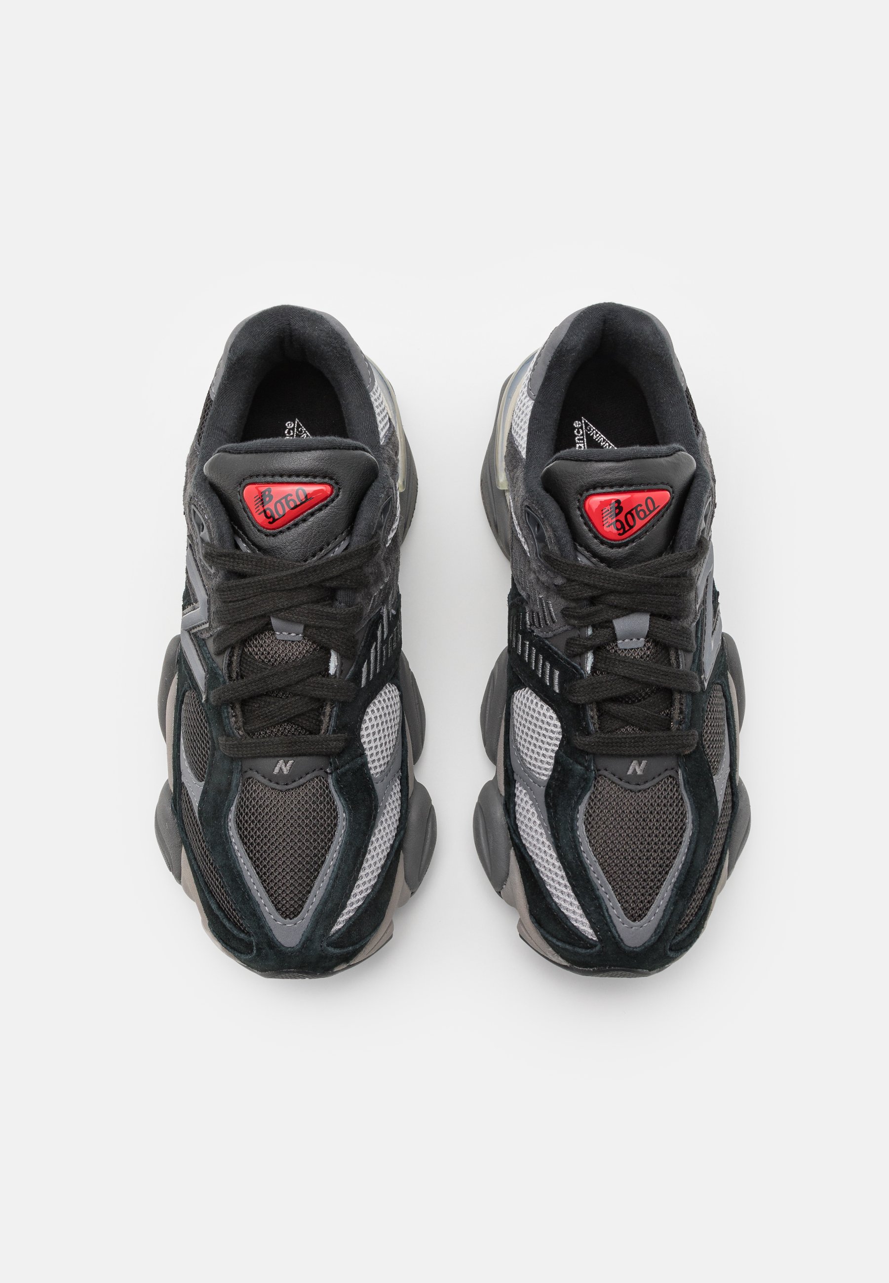 Zapatillas deportivas en negro y gris, con materiales de malla y ante, cuentan con una punta redondeada, acentos texturizados y un logotipo rojo en la lengüeta.