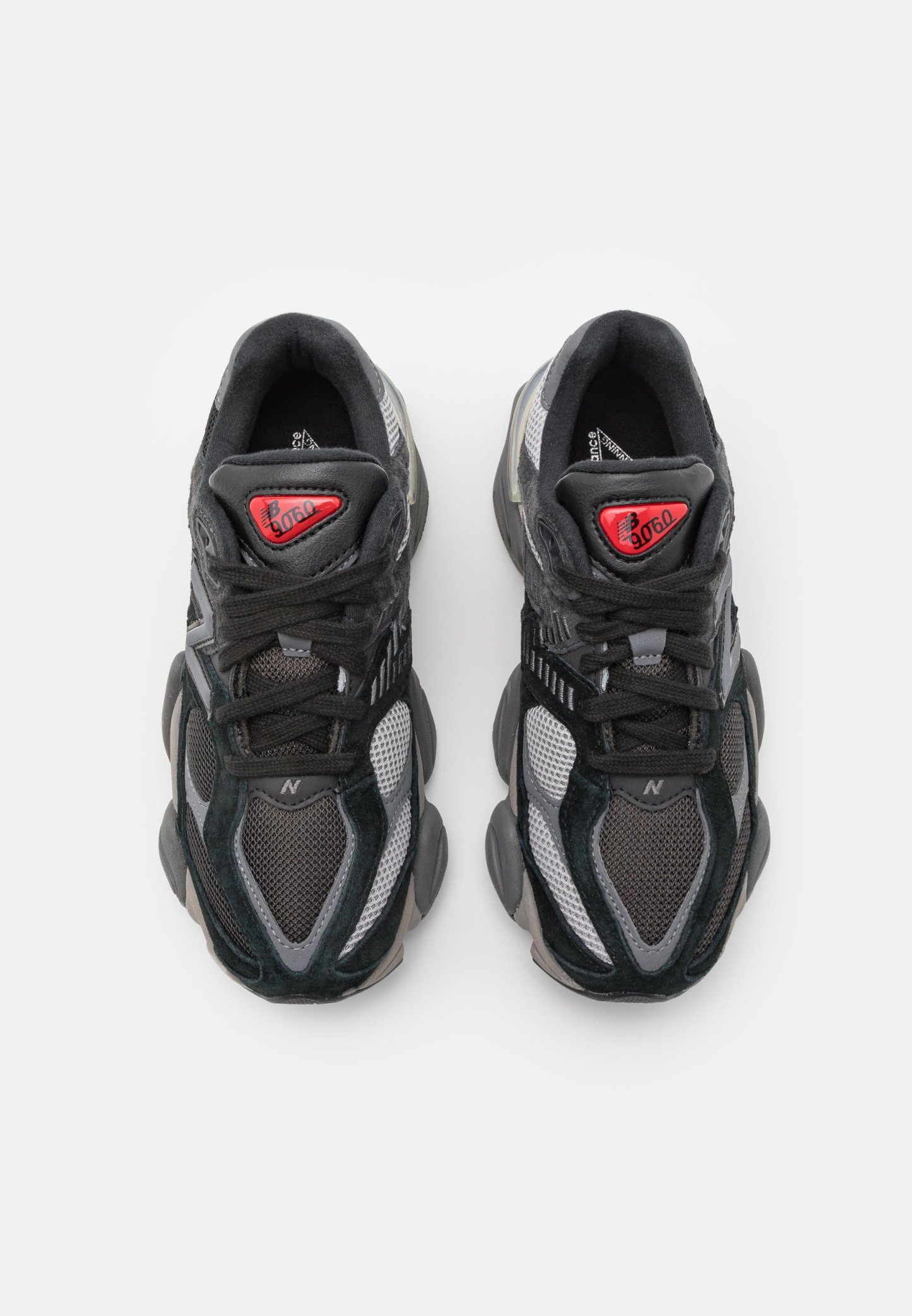 Zapatillas deportivas en negro y gris, con materiales de malla y ante, cuentan con una punta redondeada, acentos texturizados y un logotipo rojo en la lengüeta.