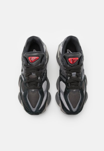 Zapatillas deportivas en negro y gris, con materiales de malla y ante, cuentan con una punta redondeada, acentos texturizados y un logotipo rojo en la lengüeta.