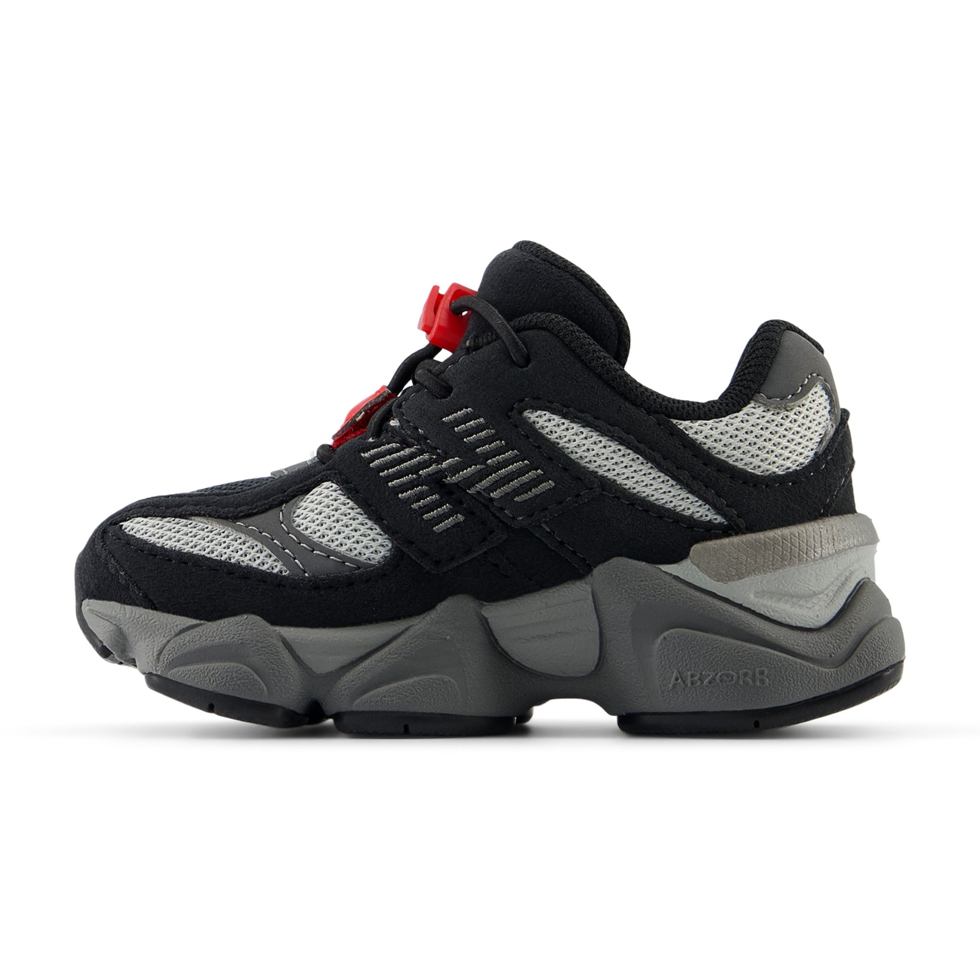 Zapatilla negra y gris con parte superior de malla y gamuza, suela de goma prominente, acento rojo en los cordones y detalles texturizados en los laterales.