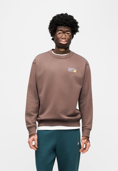 Sudadera de algodón marrón con puños y cuello acanalados, con un pequeño logo de New Balance. Combinada con pantalones deportivos azul verdoso oscuro.