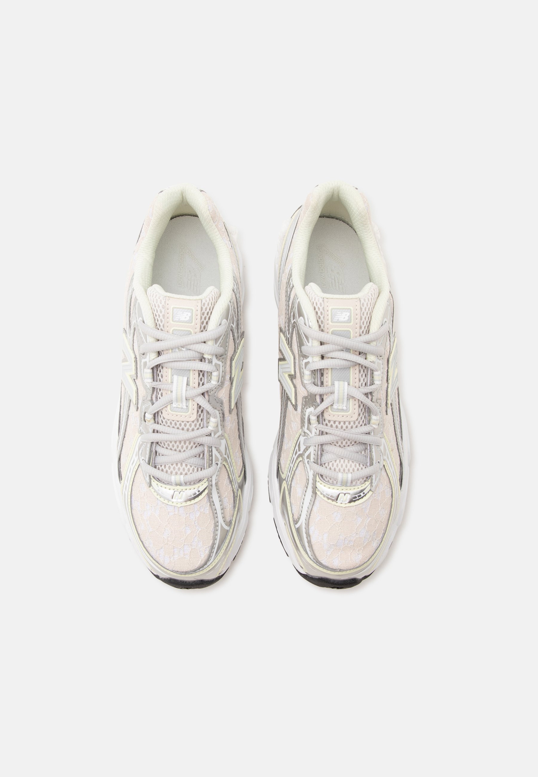 Par de zapatillas deportivas de color beige claro y blanco con cordones y detalles de malla, mostradas desde arriba sobre un fondo blanco liso.