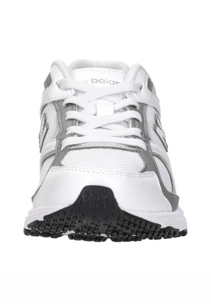 Zapatilla deportiva blanca y gris con suela negra texturizada, parte superior de malla, cordones atados y logo parcial de New Balance visible en la lengüeta y los laterales.