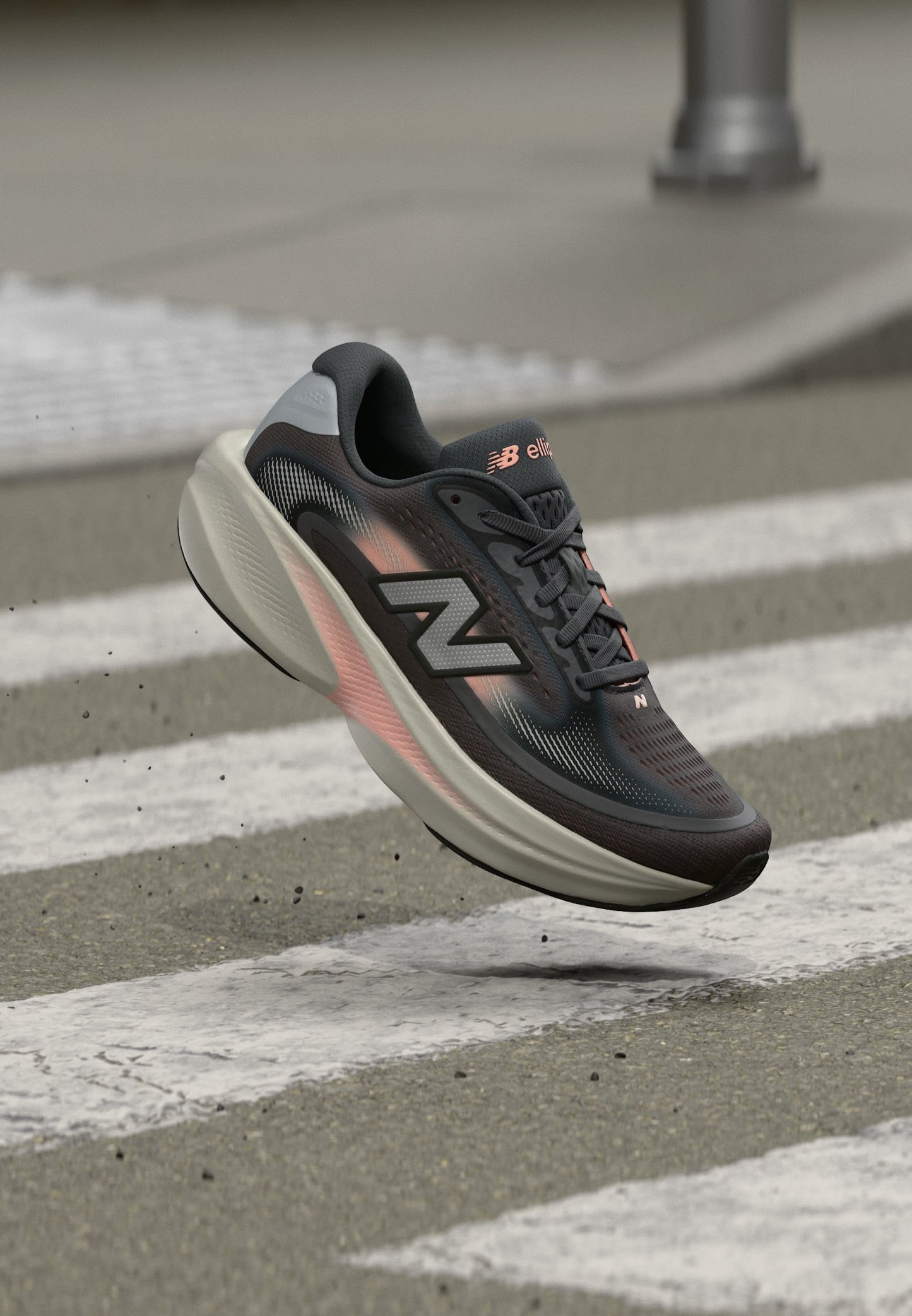 Zapatilla de correr New Balance en negro y gris con detalles en rosa flotando sobre un paso de peatones en una calle urbana.