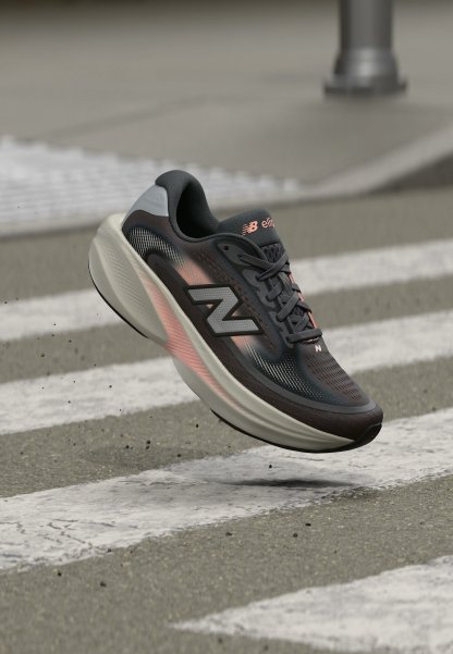 Zapatilla de correr New Balance en negro y gris con detalles en rosa flotando sobre un paso de peatones en una calle urbana.