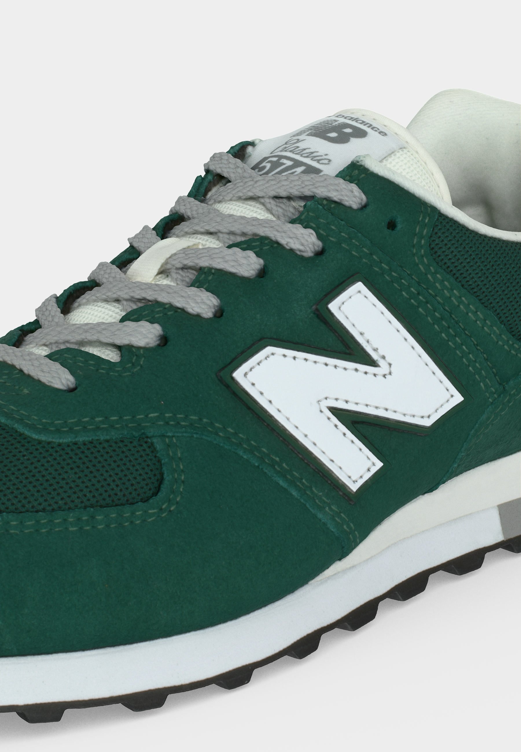 Zapatilla verde New Balance 574 con cordones grises, logotipo "N" blanco y suela blanca acolchada sobre fondo blanco.