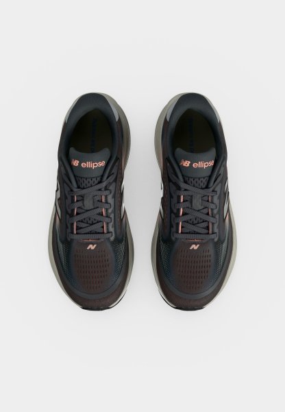 Par de zapatillas de running New Balance en gris oscuro y negro con detalles rosas y la marca "ellipse" en las lengüetas, vistas desde arriba sobre fondo blanco.
