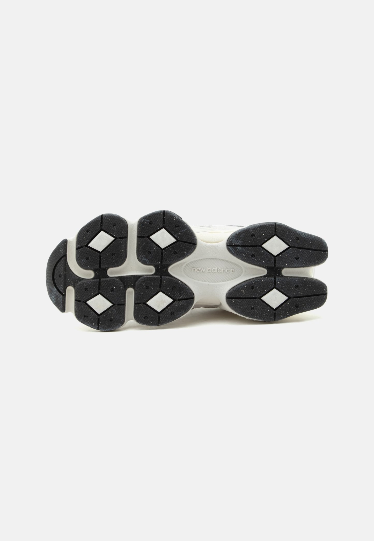 Suela de zapato New Balance blanco y negro que muestra tacos con acentos blancos en forma de diamante sobre la suela de goma negra.