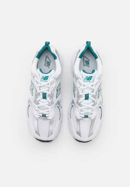 Zapatillas deportivas blancas con acentos en azul verdoso, parte superior de malla, cuello acolchado y suela de goma gruesa. Presentan elementos reflectantes y detalles del logo.