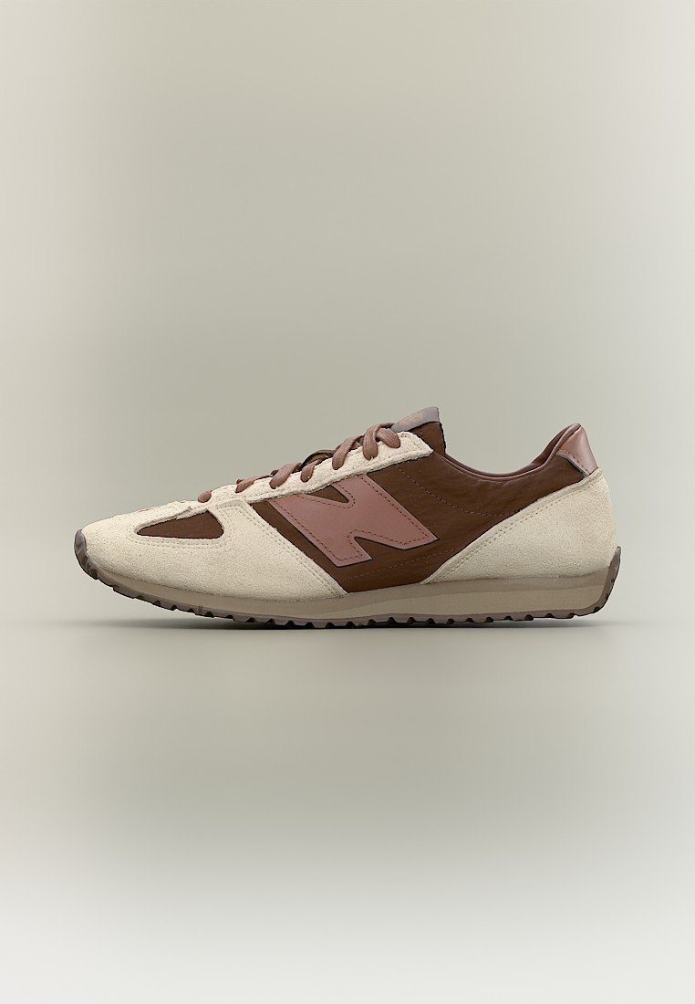 Zapatilla de perfil bajo en tonos marrón y beige, con paneles de ante y cuero, y cierre de cordones, mostrada sobre un fondo neutro.