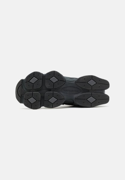 Suela de zapatilla negra con caucho texturizado, con patrones geométricos y un logotipo de marca prominente. Diseñada para ofrecer agarre y durabilidad.
