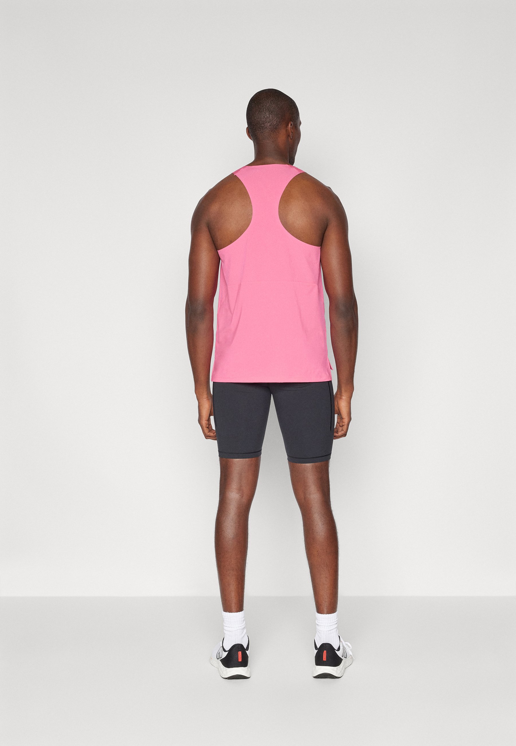 Top de tirantes rosa con un diseño de espalda nadadora, combinado con pantalones cortos negros. La tela parece ligera y de textura suave.