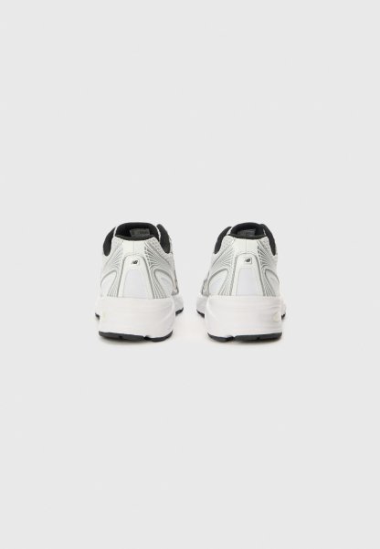 Par de zapatillas de correr blancas y grises con forro interior negro, vistas desde atrás sobre un fondo liso de color gris claro.