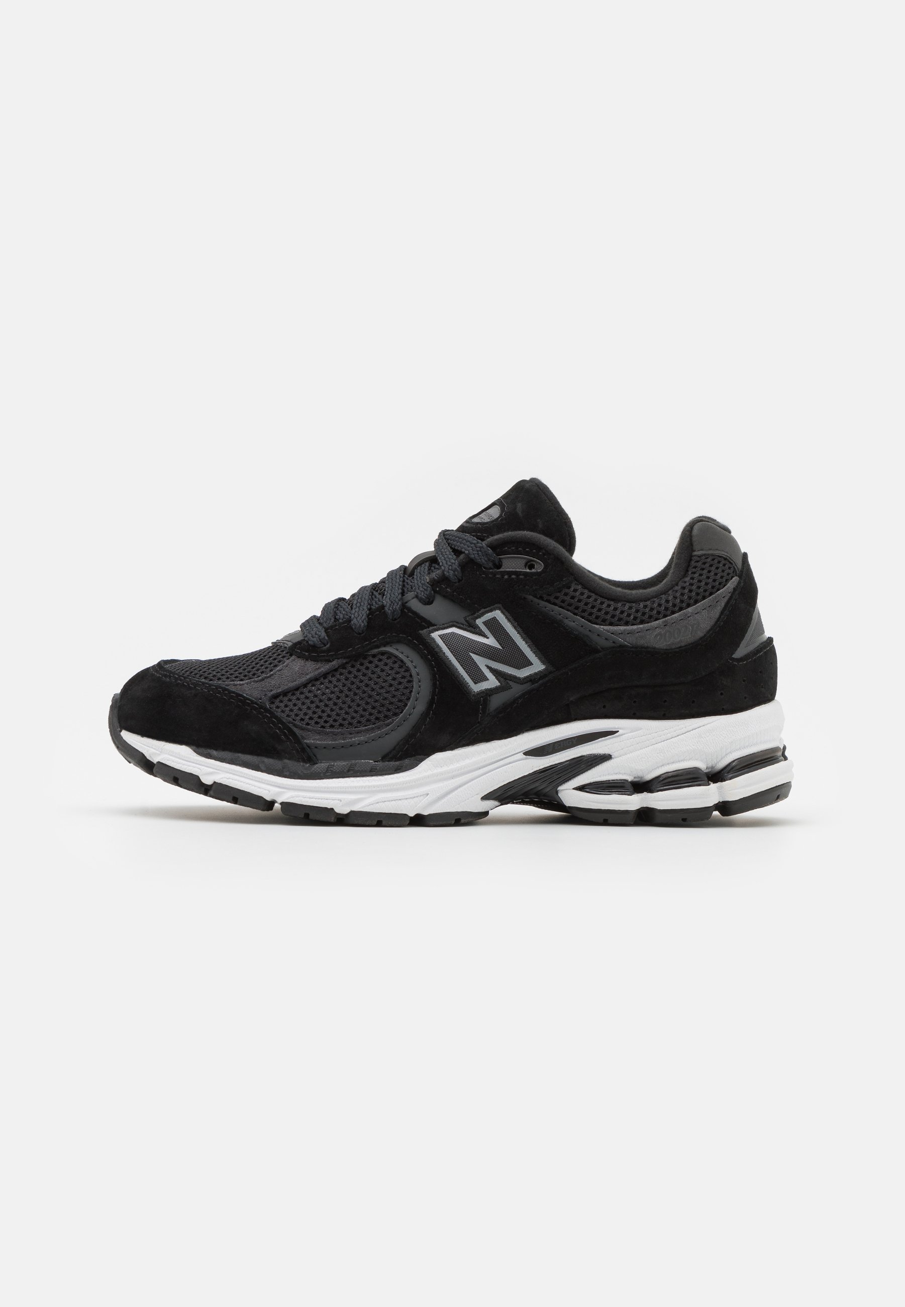 Zapatilla deportiva negra con una parte superior de malla, detalles en ante y una suela blanca texturizada con un pequeño tacón. Incluye cordones negros y un detalle del logotipo.