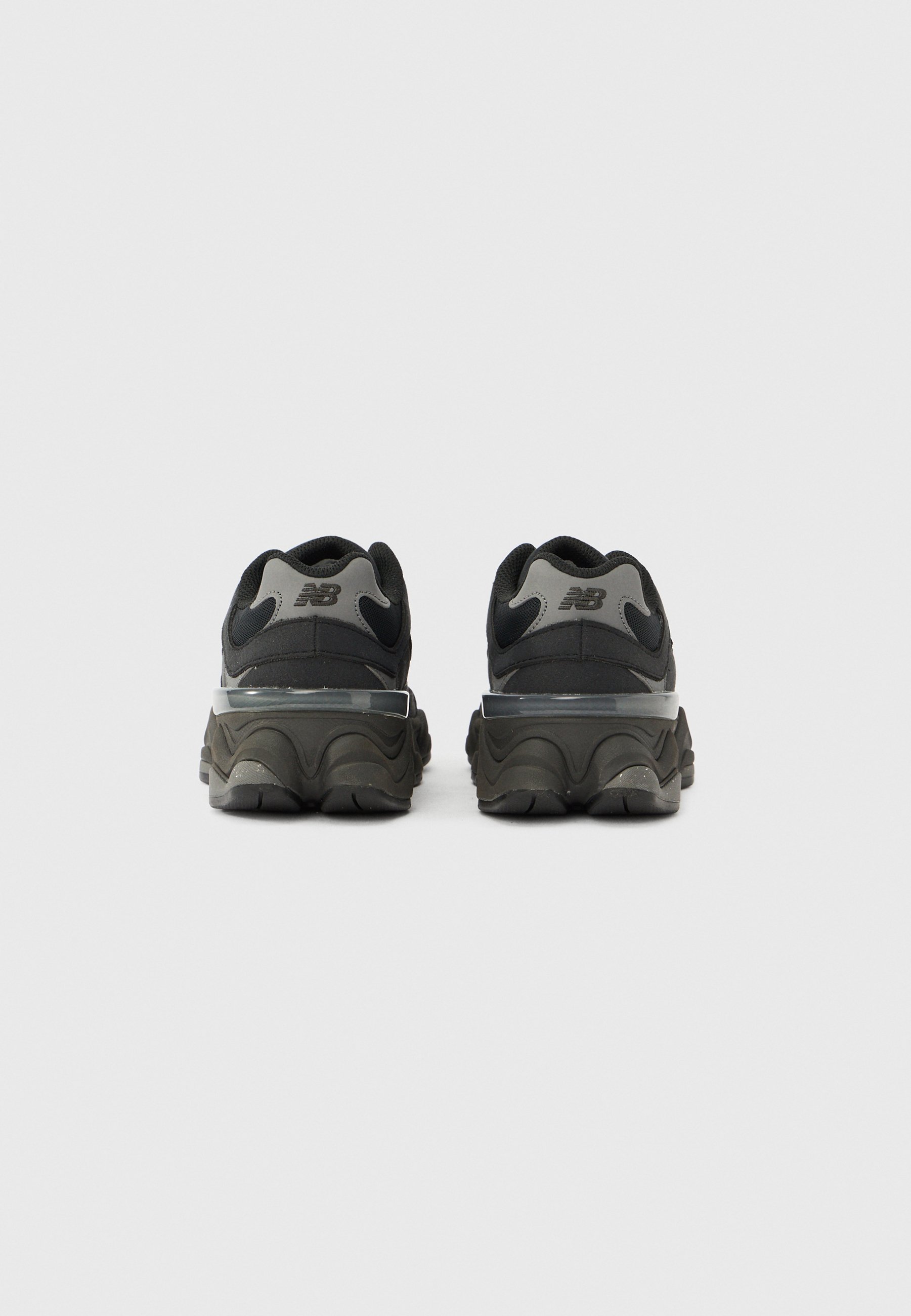 Zapatillas deportivas negras y grises con una parte superior texturizada, entresuela curva y un diseño distintivo en el talón. Presentan una marca en la parte trasera.