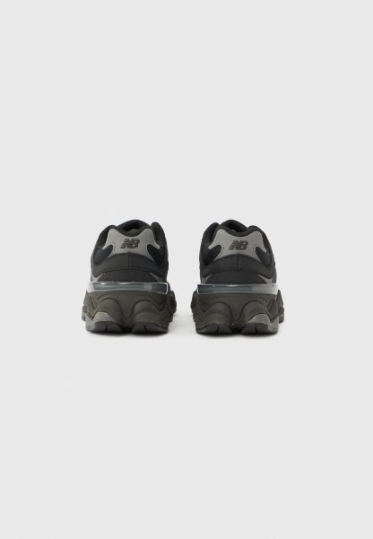 Zapatillas deportivas negras y grises con una parte superior texturizada, entresuela curva y un diseño distintivo en el talón. Presentan una marca en la parte trasera.