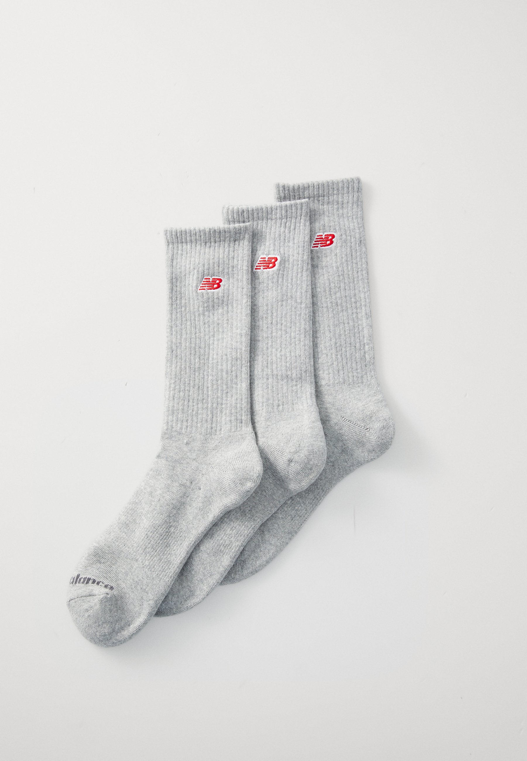 Calcetines de algodón grises con textura acanalada, que presentan detalles del logo de New Balance en rojo. Tres pares alineados para su exhibición.