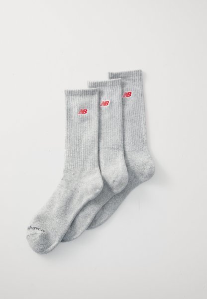 Calcetines de algodón grises con textura acanalada, que presentan detalles del logo de New Balance en rojo. Tres pares alineados para su exhibición.