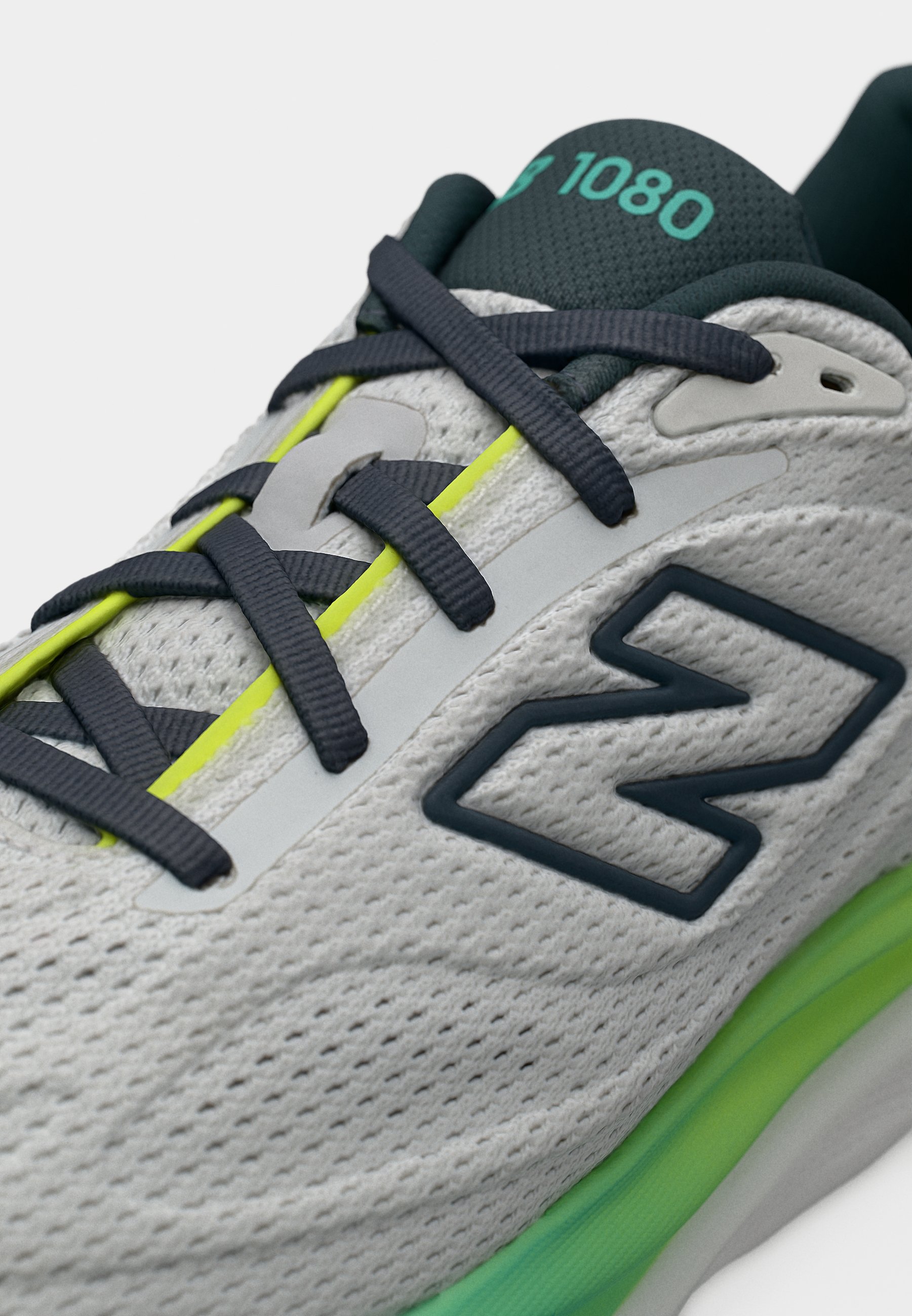 Zapato deportivo gris con cordones oscuros, detalles en verde neón, un gran logo lateral "N" y "1080" en color azul verdoso en la lengüeta negra.